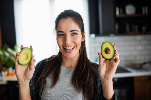 beautiful smiling young woman preparing healthy food holding avocado - loose weight imagens e fotografias de stock