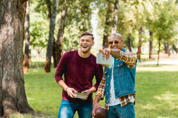 istock happy african american student pointing with finger and laughing while standing near handsome friend with books 1153041250