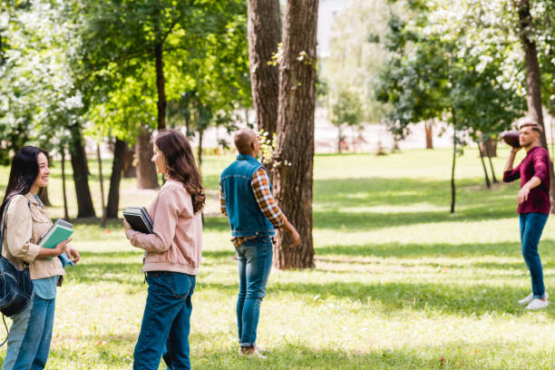 istock cheerful girls talking while standing with books near multicultural students playing american football 1153041272