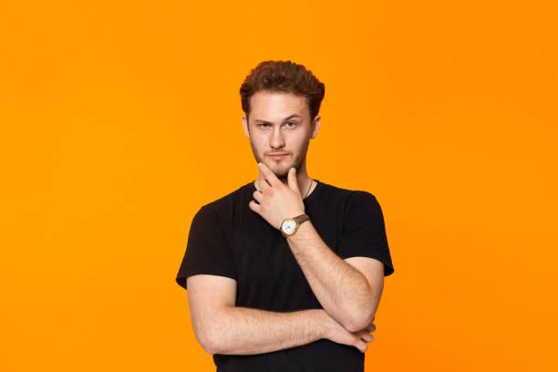 istock Young bearded confident man with hand raised on chin and looking at the camera. 1153042903