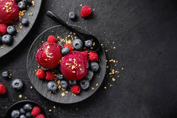 Tasty appetizing summer refreshing ice cream scoops with wild berries served on dark plate on dark background.