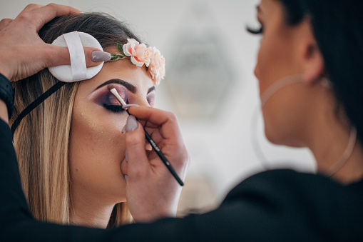 Makeup artist applying makeup on a woman with blonde hair and headband.