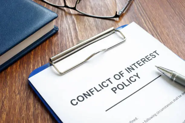 Photo of Conflict of interest policy and pen on a wooden surface.