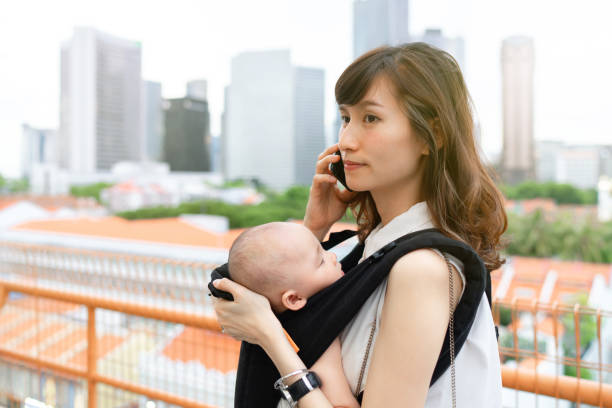 外出先で仕事をしながら、赤ちゃんと一緒に街を旅する若いアジアの中国人母 - travelogue ストックフォトと画像