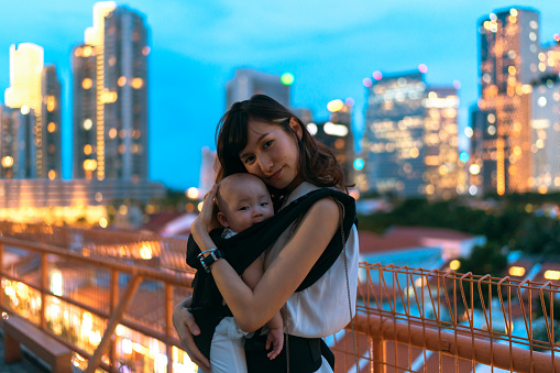 Young asian chinese mother traveling the city alone with baby in carrier