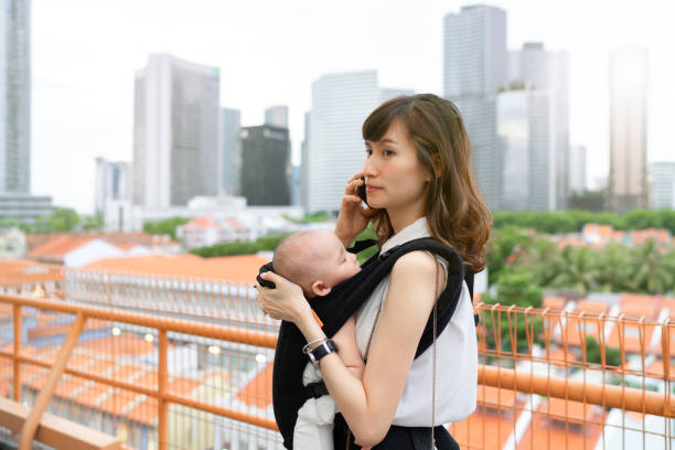 外出先で仕事をしながら、赤ちゃんと一緒に街を旅する若いアジアの中国人母 - travelogue ストックフォトと画像