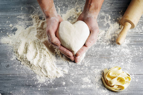 istock Heart shaped dough held by baker's hands in close-up. 1153062332