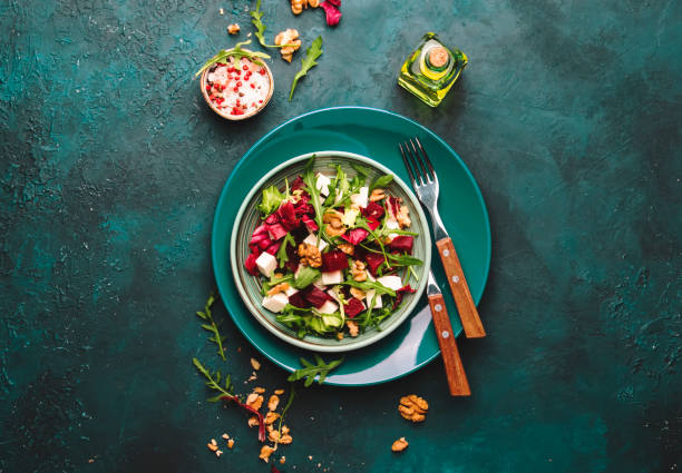 istock Beet summer salad with arugula, radicchio, soft cheese and walnuts on plate with fork, dressing and spices on blue kitchen table, copy space, top view 1153071426