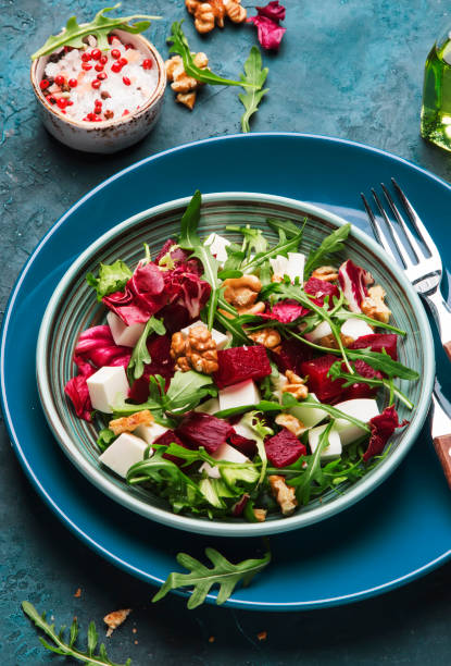 istock Beet summer salad with arugula, radicchio, soft cheese and walnuts on plate with fork, dressing and spices on blue kitchen table, copy space, top view 1153071493