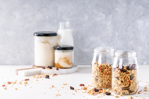Granola breakfast in glass jars served with jam, oat flakes, yogurt and milk over white texture background