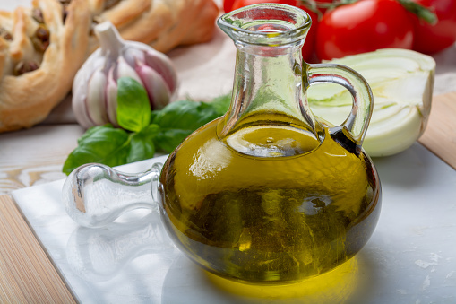 Virgin natural olive oil is glass bottle, served with traditional Mediterranean food, fresh tomatoes, olive bread, basil, fennel