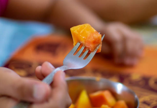 Eating papaya with fork in fingers and the table at home