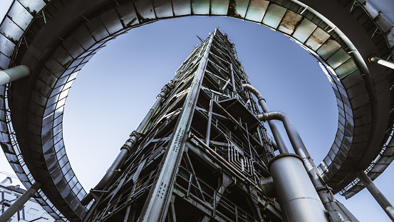 Wide angle shot from the ground of a contemporary building of an oil refinery or a modern fuel factory facility in an industrial zone, with a round bridge around, many pipes, iron beams, and tanks