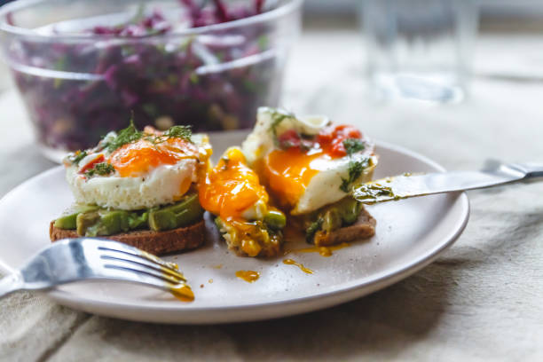 istock Breakfast served of two toasts with avocado, fried eggs with vegetables and herbs on a rustic tablecloth background. View from above. Healthy and nutritious food concept. 1153115014