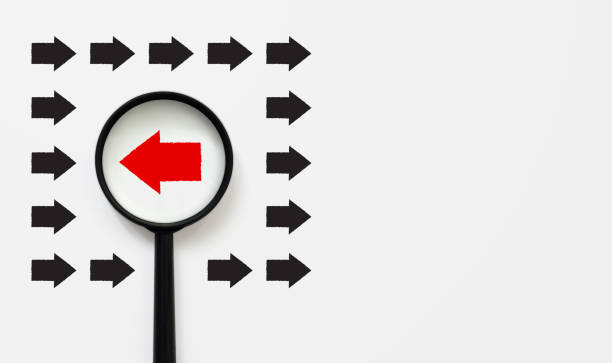 istock Magnifying glass searching for red arrow facing the opposite direction black arrows, unique, think different, individual and standing out from the crowd concept 1153130150