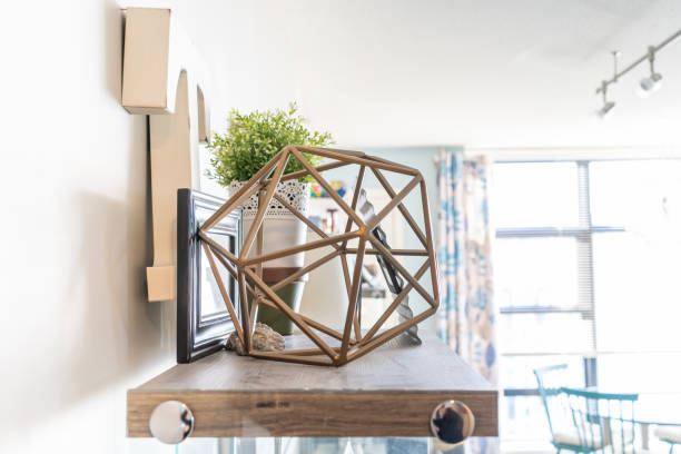 istock Home wall shelf with decorative knick knacks, including a geometric wire object, a letter 't', picture frames and a planter. Bright living room shelf. 1153141244