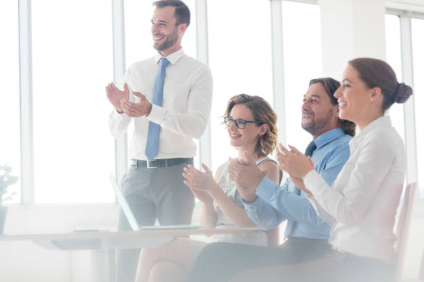 istock Smiling business colleagues applauding while sitting at table in new office during meeting 1153148741