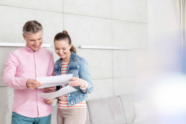 istock Smiling couple reading agreement paper while standing against wall in apartment 1153151772