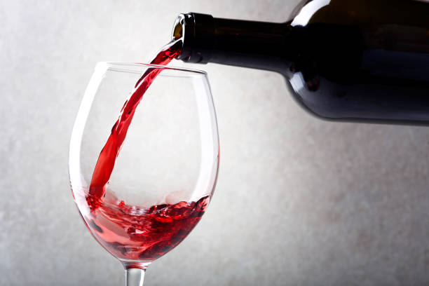 istock Red wine is poured into a glass from a bottle. Light background. 1153158143