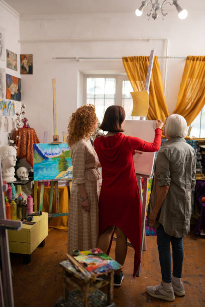 istock Aged artist looking at her students drawing on canvas 1153161182