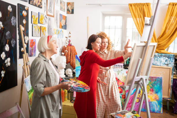 istock Grey-haired art teacher holding palette standing near students 1153161209