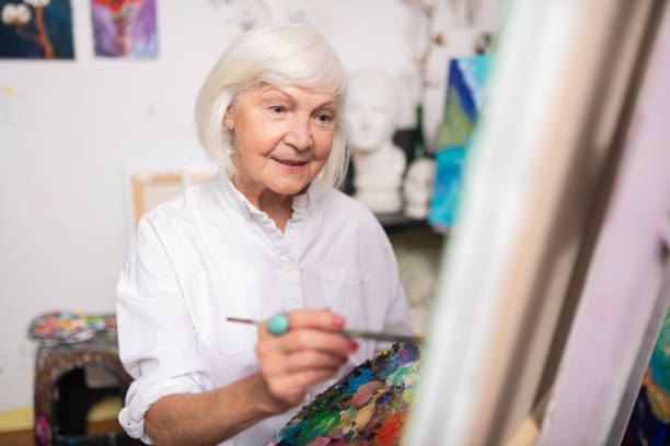 istock Appealing aged woman smiling while painting on canvas 1153161287