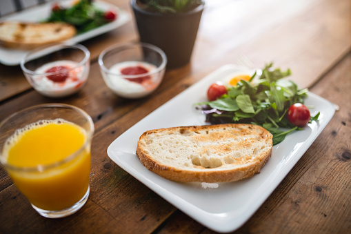 Starting the morning with delicious toasted bread, salad, yogurt, and orange juice sitting on a wooden dining table.