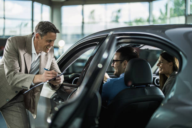 happy car salesperson talking to young couple in a showroom. - car test drive car rental women imagens e fotografias de stock