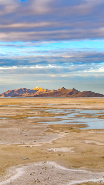 istock Vertical frame Sandy shore of a lake and distant rugged mountain under cloudy blue sky 1153173202