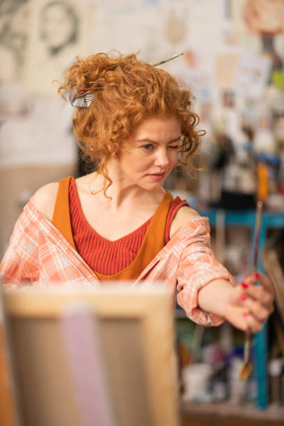 istock Curly artist looking at painting brush while working 1153173799