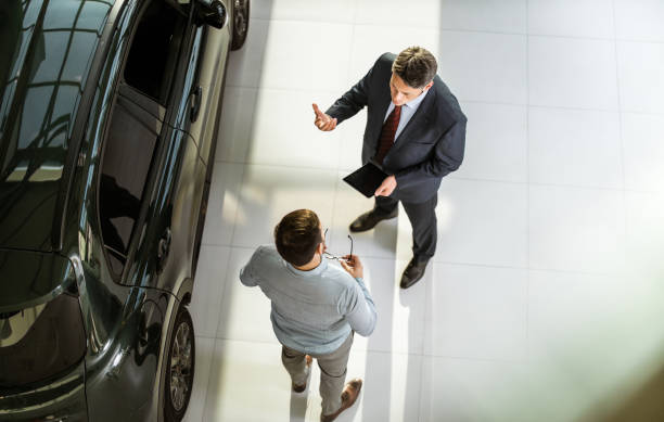 Above view of car salesperson talking to his customer in a showroom. High angle view of a salesperson using touchpad while talking to his male customer in a car showroom. Copy space. car salesperson photos stock pictures, royalty-free photos & images