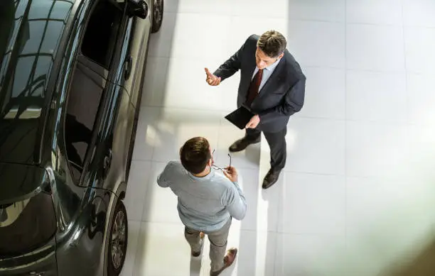 High angle view of a salesperson using touchpad while talking to his male customer in a car showroom. Copy space.