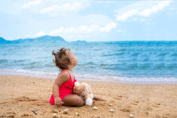 ragazza pensierosa abbraccio orsacchiotto e distogliò lo sguardo mentre era seduto in riva al mare - pensive only baby girls baby girls baby foto e immagini stock