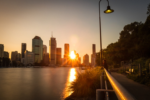Perspective view of city embankment with promenade in bright golden lights with highrise building on shore, Brisbane