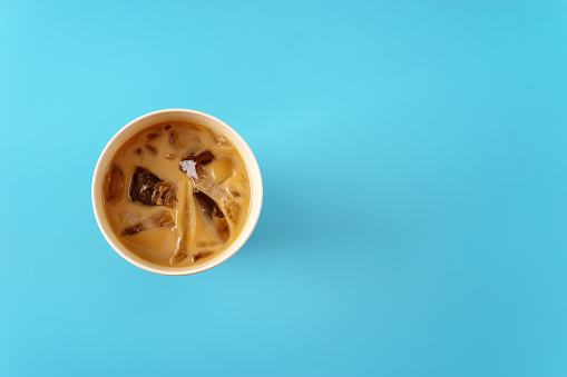 Top view of ice coffee with milk in bamboo cup on blue background