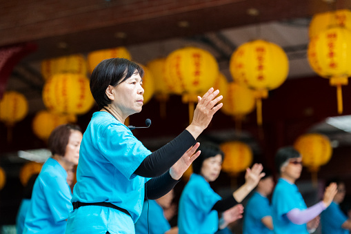 Seniors woman leads group of Tai Chi students using a microphone.