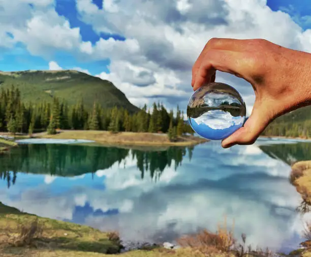 Human hand holding a glass lensball reflecting this beautiful pond surrounded by trees, near Bragg Creek, Alberta,Canada.