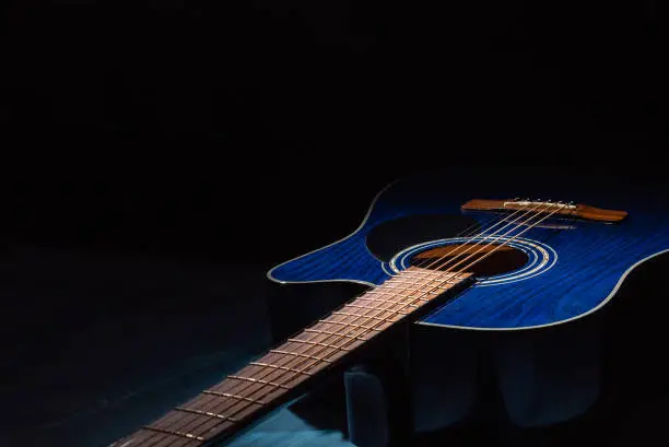 Photo of Dreadnought acoustic guitar on a blue wooden background in the dark.