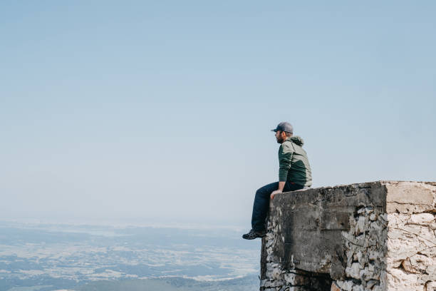 istock Man with cap  sitting backside looking view from top of building. 1153230295