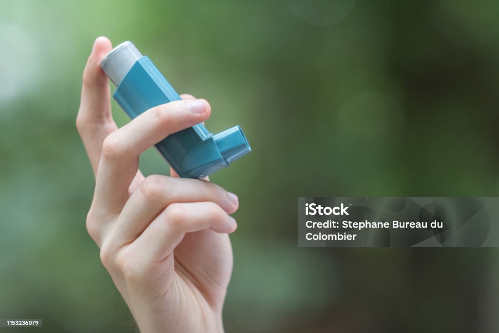 Asthma medecine inhaler holded by a man View of a man's hand holding a blue asthma inhaler Asthmatic Stock Photo