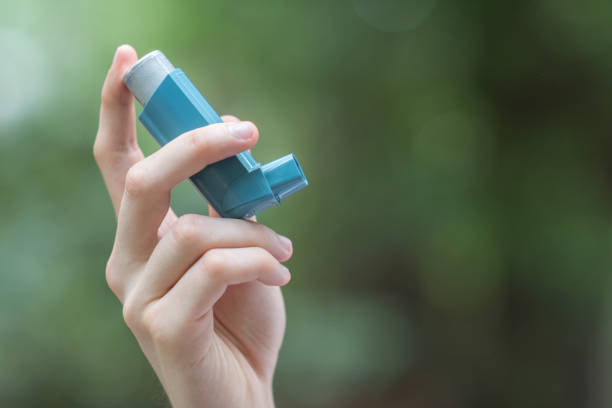 Asthma medecine inhaler holded by a man View of a man's hand holding a blue asthma inhaler flower part stock pictures, royalty-free photos & images