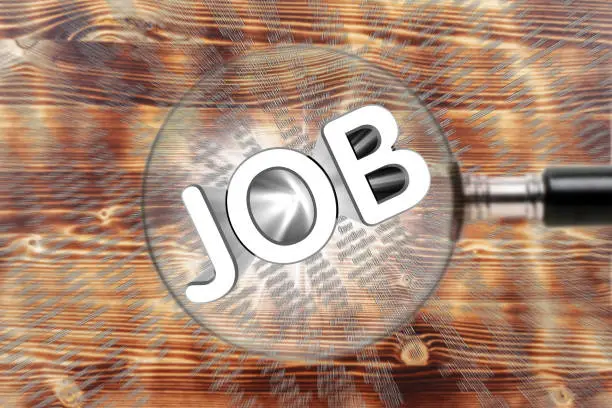 JOB word through a magnifying glass on an wooden background. Job search concept.