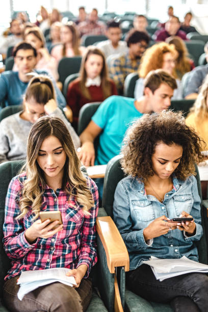 istock Female college students using mobile phones during a class at lecture hall. 1153242320