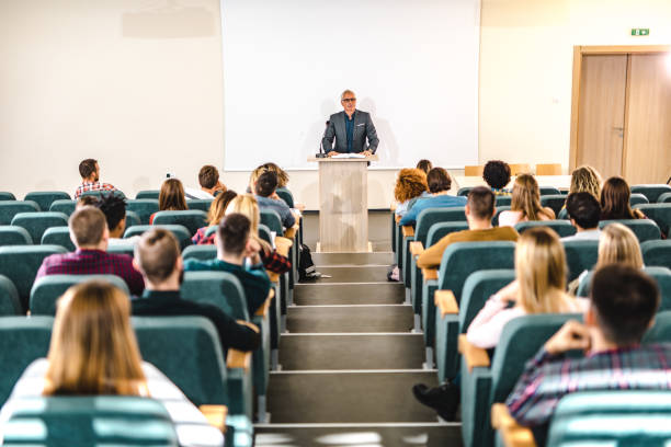 istock Mature professor giving a lecture in front of projection screen at lecture hall. 1153243206