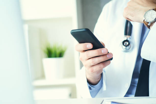istock Male doctor in white coat is using a modern smartphone device with touch screen. Doctor hands with mobile phone. 1153245259