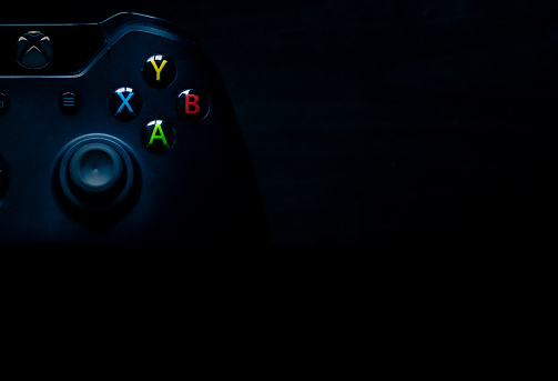 SHEFFIELD, UK - JUNE 2ND 2019: Shot taken overhead of half a black Microsoft Xbox One controller with emphasis on the colourful buttons sitting on the left of a dark black background, perfect for presentation material like powerpoints