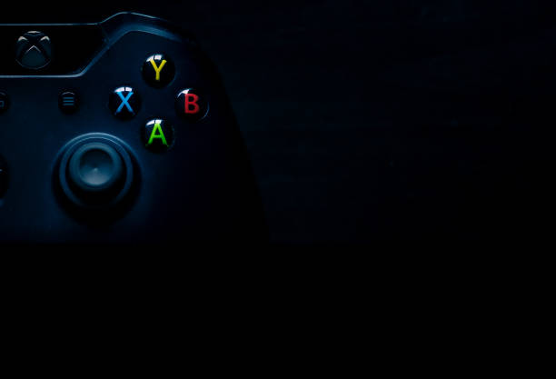 The Xbox one controller sits in the corner of the image as presentation material SHEFFIELD, UK - JUNE 2ND 2019: Shot taken overhead of half a black Microsoft Xbox One controller with emphasis on the colourful buttons sitting on the left of a dark black background, perfect for presentation material like powerpoints microsoft stock pictures, royalty-free photos & images