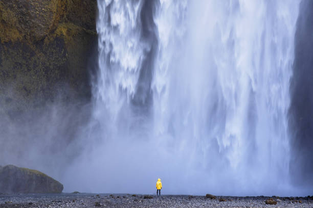istock Man dressed in a raincoat looks at a powerful waterfall in Iceland 1153247699