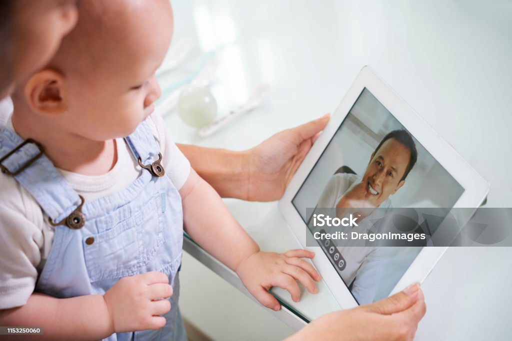 Donna con baby videochia chiamata marito - Foto stock royalty-free di Telemedicina