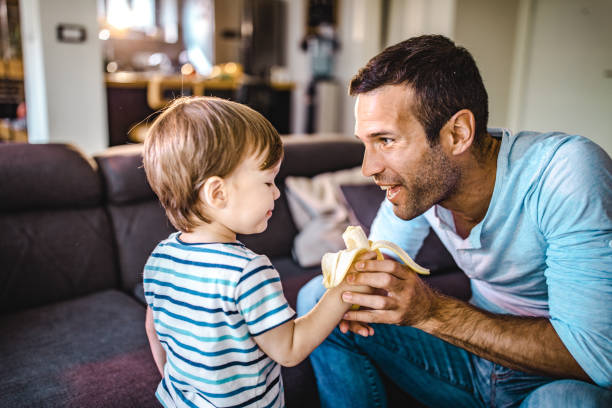 istock Young happy father feeding his small boy with banana. 1153251931